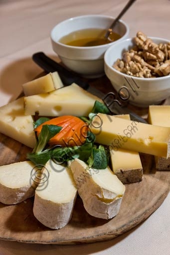 Piatto di formaggi valtellinesi, miele e noci su tagliere di legno