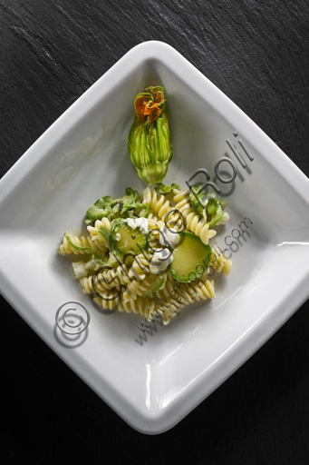 A dish of rotini pasta with zucchini and melted mozzarella cheese, garnished with basil.