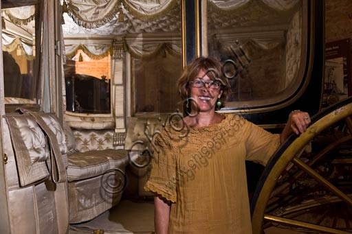 Antonella Gigli, director of the Farnese Municipal Museums, beside a historic carriage in the Carriage Museum at Farnese Palace, Piacenza