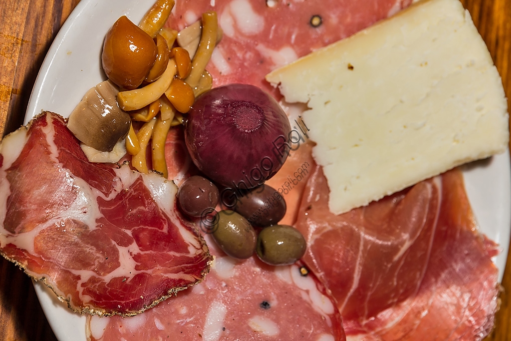 Assortimento di prodotti tipici toscani: salumi, olive in salamoia e pecorino su tagliere di legno.