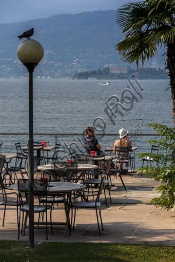 Photograph of Stresa lakefront with tourists at a table, pigeon on lamppost, and view of Isola Madre, Lake Maggiore