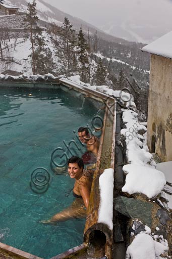 Coppia di ospiti nella piscina termale all'aperto dei Bagni Vecchi di Bormio, con lo sfondo delle montagne alpine