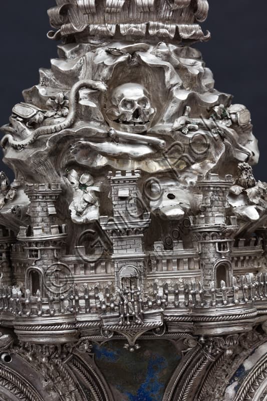 Dettaglio Croce di San Giovanni, Museo Duomo Firenze: particolare centro con edifici città, serpente e teschio su sfondo argento cesellato.