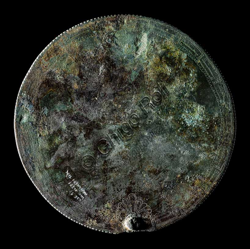 Museo Civico Archeologico di Bologna: specchio in bronzo, dalla necropoli Arnoaldi, tomba 104.Gli specchi etruschi sono costituiti da un disco di bronzo ben lucidato sul lato destinato a riflettere l'immagine e spesso decorato sul retro con incisioni, o più raramente con rilievi, che rappresentano scene di toilette o figure mitologiche.Questo esemplare, proviene da una ricca tomba femminile purtroppo giunta a noi già saccheggiata, forse in epoca romana.La decorazione è realizzata su entrambe le facce: sul lato riflettente sono incise una palmetta, in basso, e due fasce concentriche, lungo il bordo; sul retro dello specchio è raffigurato un guerriero vestito con tunica e calzari a punta, e con elmo a calotta, intento a suonare il corno. Ai lati del guerriero sono raffigurati due mostri di natura fantastica.Lo specchio è considerato di tipo etrusco e di produzione bolognese, poi istoriato da un artista di area veneto-alpina, ispirato alle raffigurazioni tipiche dell'"arte delle situle".Prima metà del V secolo a.C.Inventario: 16291.