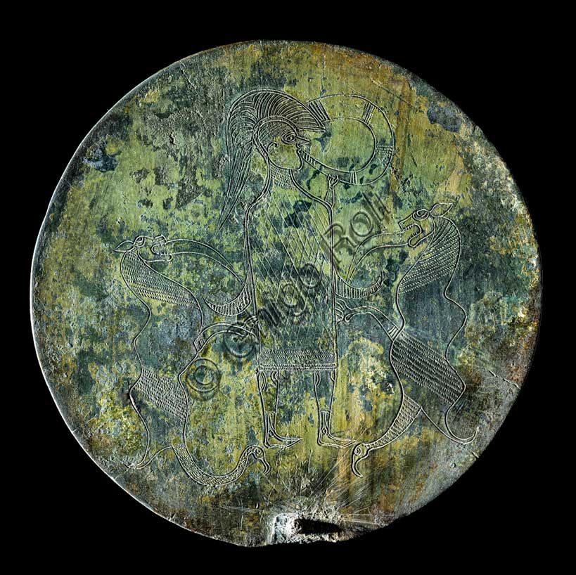 Museo Civico Archeologico di Bologna: specchio in bronzo, dalla necropoli Arnoaldi, tomba 104.Gli specchi etruschi sono costituiti da un disco di bronzo ben lucidato sul lato destinato a riflettere l'immagine e spesso decorato sul retro con incisioni, o più raramente con rilievi, che rappresentano scene di toilette o figure mitologiche.Questo esemplare, proviene da una ricca tomba femminile purtroppo giunta a noi già saccheggiata, forse in epoca romana.La decorazione è realizzata su entrambe le facce: sul lato riflettente sono incise una palmetta, in basso, e due fasce concentriche, lungo il bordo; sul retro dello specchio è raffigurato un guerriero vestito con tunica e calzari a punta, e con elmo a calotta, intento a suonare il corno. Ai lati del guerriero sono raffigurati due mostri di natura fantastica.Lo specchio è considerato di tipo etrusco e di produzione bolognese, poi istoriato da un artista di area veneto-alpina, ispirato alle raffigurazioni tipiche dell'"arte delle situle".Prima metà del V secolo a.C.Inventario: 16291.