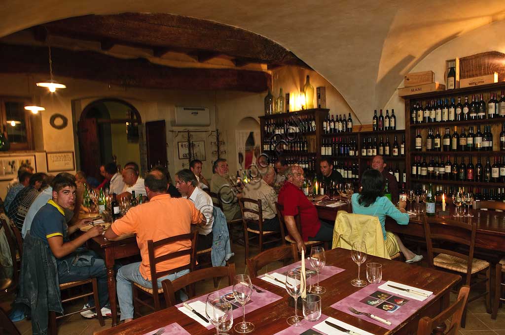 Bevagna, la "Bottega Di Piazza Onofri", enoteca e ristorante: scaffali con bottiglie di vino rosso e clienti ai tavoli.