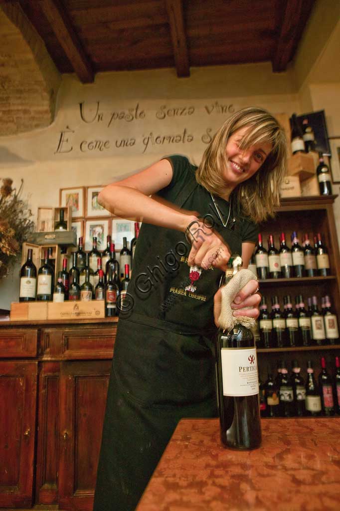 Bevagna, la "Bottega Di Piazza Onofri", enoteca e ristorante: una cameriera stappa una bottiglia di vino rosso.