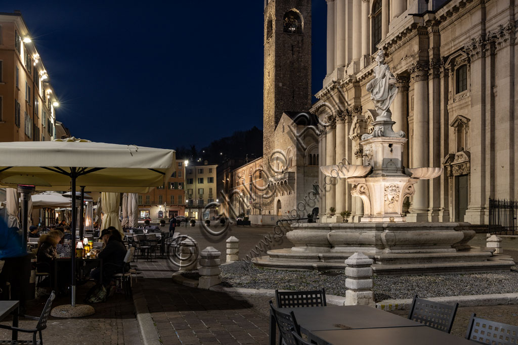 Brescia, Paolo VI Square: night view. From the left, the Broletto with the Pégol Tower and the Loggia delle Grida; and part of the facade of the Duomo Nuovo  (the New Cathedral) , in late Baroque style with the facade of Botticino marble. In the foreground, the fountain with a copy of the neoclassical statue of Minerva, known as "Armed Brescia".