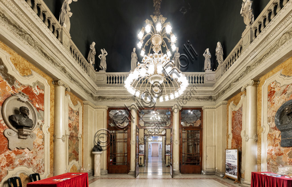 Brescia, Teatro Grande: Hall of the Statues. The current appearance of the room consists of a peristyle with smooth stuccoed columns and Ionic capitals and four angular pillars supporting an architraved system with a balustrade surmounted by 16 plaster statues and plastered canvas by Giuseppe Luzziardi.