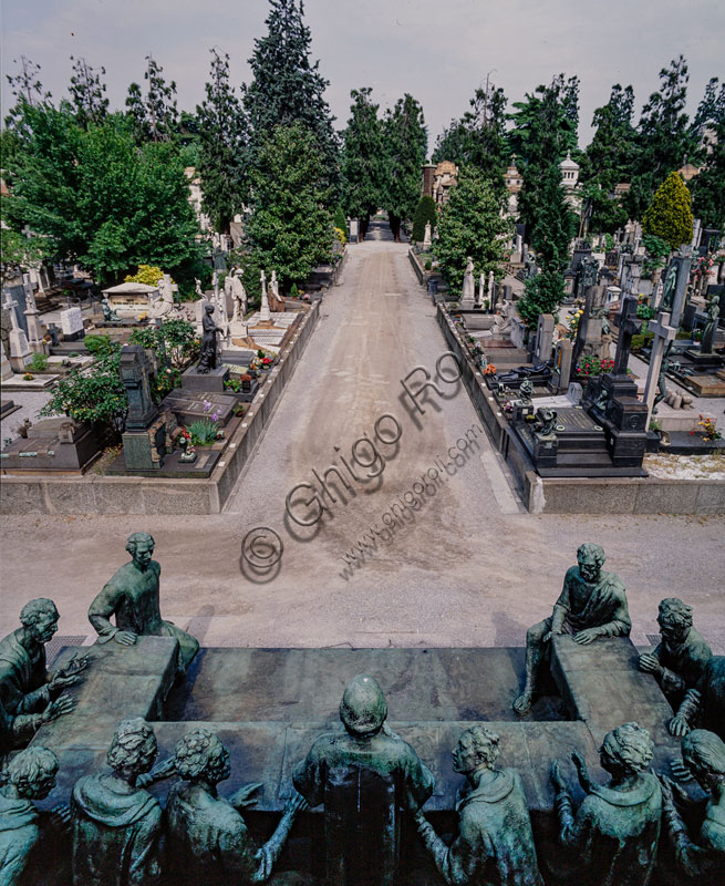 Cimitero Monumentale: veduta del cimitero. In primo piano, l’edicola Campari, con il gruppo scultoreo in bronzo  “L’Ultima Cena” di Giannino Castiglioni (1935) posto su un basamento ricavato da un masso erratico porfirico. Il monumento funebre viene eretto (1936-1939) per volontà di Davide Campari (1867-1936), titolare dell’omonima azienda produttrice di bevande e liquori, il cui padre Gaspare intorno al 1865 aveva iniziato la produzione dell’amaro “bitter” a Milano.