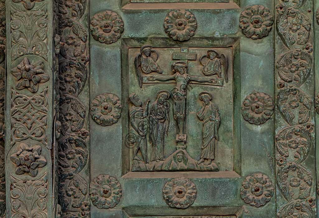 Duomo di Monreale, Porta di Bonanno Pisano (1185-6): formella bronzea con "Crocifissione" (scena dal Nuovo Testamento).La porta è firmata: "Bonanno civis pisanus". Iconograficamente nei cinque ordini inferiori vi sono scene del Vecchio Testamento, sette dedicate alla storia di Adamo ed Eva, e altre sei ad altrettante coppie di profeti mentre nei cinque superiori scene del Nuovo, al sommo Cristo e Maria nella gloria del Paradiso.