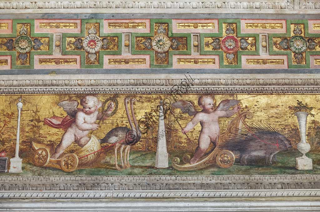 Ferrara, Castello Estense (detto anche Castello di San Michele): particolare dei cornicioni  decorati con putti alla guida di bighe fantastiche e festoni di frutta in campo d'oro.Opera di Leonardo da Brescia. La sala, già stanza privata di Ercole II, era conosciuta nel Cinquecento come camera dello specchio. Da essa prende il nome l'intero appartamento di rappresentanza voluto da Alfonso II.Le scene proposte nella volta di questa sala vengono oggi generalmente interpretate come un'allegoria della vita umana.