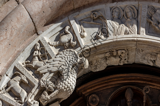 Foligno, Cattedrale di San Feliciano, la facciata: il portale. Particolare del fregio. Il portale centrale, opera dei maestri Rodolfo e Binello, mostra un disco solare nella lunetta, in cui si trova l'iscrizione con la data 1201, anno del completamento della facciata; nella facciata interna degli stipiti si trovano poi i rilievi con l'Imperatore Ottone IV di Brunswick e papa Innocenzo III, mentre il giro interno dell'arco è decorato dai Simboli degli evangelisti e i Segni dello zodiaco; nel giro esterno una fascia di mosaici cosmateschi. Il portale ligneo intagliato è del 1620. 