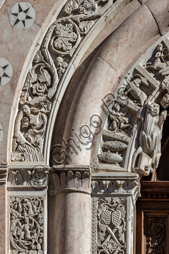 Foligno, Cattedrale di San Feliciano, la facciata: il portale. Particolare del fregio. Il portale centrale, opera dei maestri Rodolfo e Binello, mostra un disco solare nella lunetta, in cui si trova l'iscrizione con la data 1201, anno del completamento della facciata; nella facciata interna degli stipiti si trovano poi i rilievi con l'Imperatore Ottone IV di Brunswick e papa Innocenzo III, mentre il giro interno dell'arco è decorato dai Simboli degli evangelisti e i Segni dello zodiaco; nel giro esterno una fascia di mosaici cosmateschi. Il portale ligneo intagliato è del 1620. 