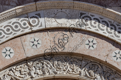  Foligno, Cathedral of  St. Feliciano, the façade:  the entrance door. Detail of the frieze of  the portal. The central portal, work of the masters Rodolfo and Binello, shows a solar disk in the lunette, in which there is the inscription with the date 1201, the year of completion of the facade; in the inner façade of the jambs there are then the reliefs with the Emperor Otto IV of Brunswick and Pope Innocent III, while the inner circle of the arch is decorated by the symbols of the evangelists and the Signs of the zodiac; in the outer circle a band of cosmatesque mosaics. The carved wooden portal was made in 1620.