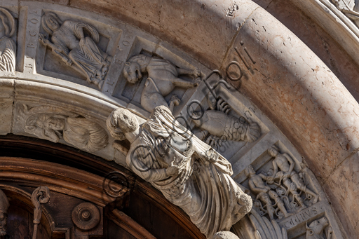  Foligno, Cathedral of  St. Feliciano, the façade:  the entrance door. Detail of the frieze of  the portal. The central portal, work of the masters Rodolfo and Binello, shows a solar disk in the lunette, in which there is the inscription with the date 1201, the year of completion of the facade; in the inner façade of the jambs there are then the reliefs with the Emperor Otto IV of Brunswick and Pope Innocent III, while the inner circle of the arch is decorated by the symbols of the evangelists and the Signs of the zodiac; in the outer circle a band of cosmatesque mosaics. The carved wooden portal was made in 1620.