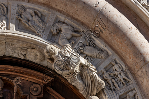 Foligno, Cattedrale di San Feliciano, la facciata: il portale. Particolare del fregio. Il portale centrale, opera dei maestri Rodolfo e Binello, mostra un disco solare nella lunetta, in cui si trova l'iscrizione con la data 1201, anno del completamento della facciata; nella facciata interna degli stipiti si trovano poi i rilievi con l'Imperatore Ottone IV di Brunswick e papa Innocenzo III, mentre il giro interno dell'arco è decorato dai Simboli degli evangelisti e i Segni dello zodiaco; nel giro esterno una fascia di mosaici cosmateschi. Il portale ligneo intagliato è del 1620. 