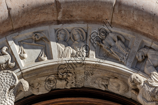 Foligno, Cattedrale di San Feliciano, la facciata: il portale. Particolare del fregio. Il portale centrale, opera dei maestri Rodolfo e Binello, mostra un disco solare nella lunetta, in cui si trova l'iscrizione con la data 1201, anno del completamento della facciata; nella facciata interna degli stipiti si trovano poi i rilievi con l'Imperatore Ottone IV di Brunswick e papa Innocenzo III, mentre il giro interno dell'arco è decorato dai Simboli degli evangelisti e i Segni dello zodiaco; nel giro esterno una fascia di mosaici cosmateschi. Il portale ligneo intagliato è del 1620. 