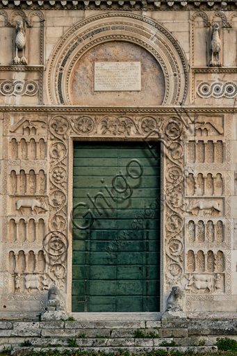 Spoleto, Chiesa di San Pietro: la facciata, caratterizzata da rilievi romanici (XII secolo). Particolare del portale maggiore. Tale portale è sormontato da una lunetta a ferro di cavallo, fiancheggiata da due aquile e da decorazioni cosmatesche. Ai lati degli stipiti si trovano quattro ordini di archetti decorativi su colonnine con sfondo di fiori, animali stilizzati e figure geometriche, intercalati a due a due da sculture simboliche a pieno rilievo (il lavoratore con i buoi e il cane, la cerva che allatta il suo nato e divora una serpe, il pavone che becca uva).