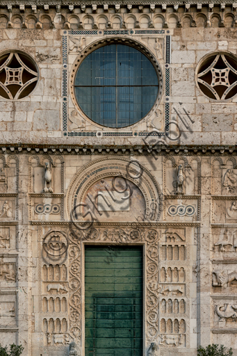 Spoleto, Chiesa di San Pietro: la facciata, caratterizzata da rilievi romanici (XII secolo). Particolare della parte mediana con l'oculo centrale (che è inquadrato da da una decorazione cosmatesca e circondato da simboli degli Evangelisti) e il portale maggiore. Tale portale è sormontato da una lunetta a ferro di cavallo, fiancheggiata da due aquile e da decorazioni cosmatesche. Ai lati degli stipiti si trovano quattro ordini di archetti decorativi su colonnine con sfondo di fiori, animali stilizzati e figure geometriche, intercalati a due a due da sculture simboliche a pieno rilievo (il lavoratore con i buoi e il cane, la cerva che allatta il suo nato e divora una serpe, il pavone che becca uva).