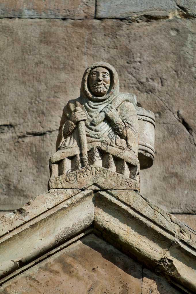 Fidenza, Duomo (Cattedrale di S. Donnino), Facciata, acroterio del portale di destra: la figura di Raimondinus vilis. Una scritta lo identifica come Raimondinus vilis (l'umile Raimondino) sulla cui identità vi sono più dubbi che certezze. Diverse ipotesi lo qualificano come: un povero romeo morto a Borgo San Donnino; un personaggio diventato simbolo della povera gente che ha contribuito manualmente ai lavori di edificazione della chiesa; San Raimondino da Piacenza, un santo pellegrino.Bassorilievo di Benedetto Antelami e bottega.