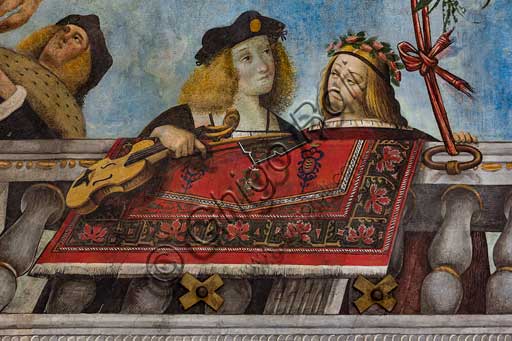 Ferrara, Palazzo Costabili or Palazzo di Ludovico il Moro (today it is the seat of the National Archaeological of Spina), Aula Costabiliana o Hall of the Treasure, vault, XVI century frescoes by  Benvenuto Tisi, known as  il Garofalo: detail with gentleman holding a musical instrument and a gentlewoman. Along the sides of the ceiling a large balcony, where Oriental rugs are hanging out, is painted. There is a gallery of characters, many of them have musical instruments. They leanfrom the balcony and show the observers their love for arts, music and poetry. The ceiling is almost a showcase of the aristocracy of the time with portraits of rare elegance.  In an evocative scenography, above the balcony, there are a turquoise sky , with a gazebo filled with branches of fruit, knotted around the balustrade. This room is, in fact, a hortus conclusus, a secret garden realised by the owner for his notable guests.At the centre  there are a magnificent rose window in carved and gilded wood, and a painted architecture that is used both as a decoration and as a cover.  All around runs a frieze that goes all around the room, with grotesque medallions depicting with scenes taken from mythology and stories of ancient Rome.