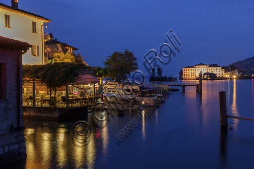   Isola Pescatori: the lakefront with a pier of a restaurant and some boats. In the background, night view of Isola Bella with the illuminated Borromeo Palace.