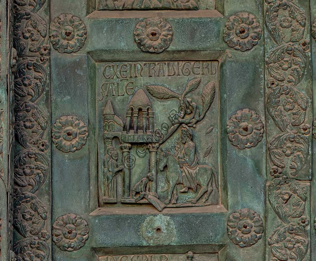 Duomo di Monreale, Porta di Bonanno Pisano (1185-6): formella bronzea con "L'entrata a Gerusalemme" (scena dal Nuovo Testamento).La porta è firmata: "Bonanno civis pisanus". Iconograficamente nei cinque ordini inferiori vi sono scene del Vecchio Testamento, sette dedicate alla storia di Adamo ed Eva, e altre sei ad altrettante coppie di profeti mentre nei cinque superiori scene del Nuovo, al sommo Cristo e Maria nella gloria del Paradiso.