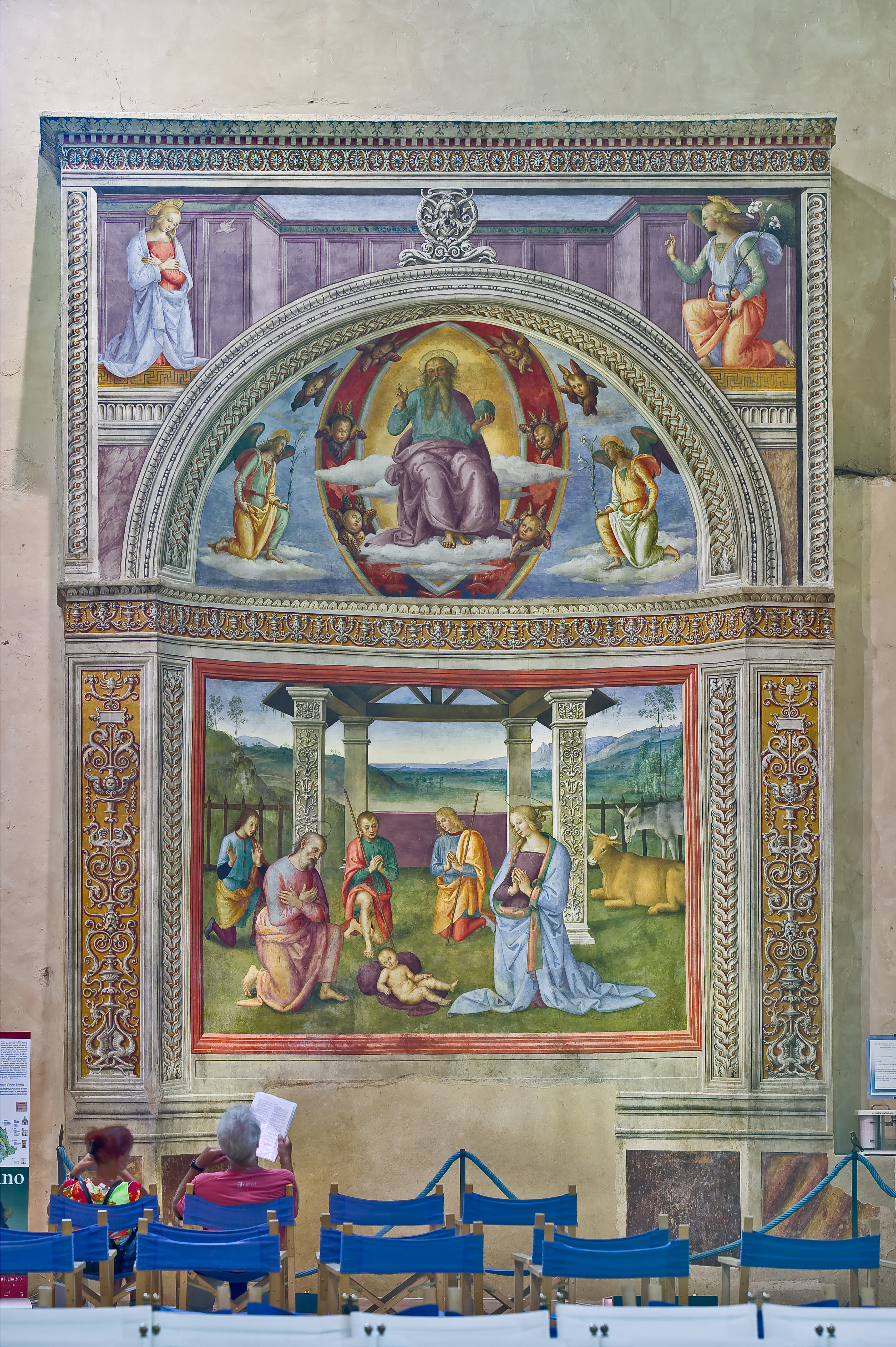 Montefalco, Museum of St. Francis, Church of St. Francis: "Nativity with the Annunciation and the Eternal among angels and cherubs", by Pietro Vannucci known as  Perugino, 1503. Fresco. From the top, "Annunciation", "The blessing Eternal between cherubs and two kneeling angels", "Nativity". Works admired by two tourists.