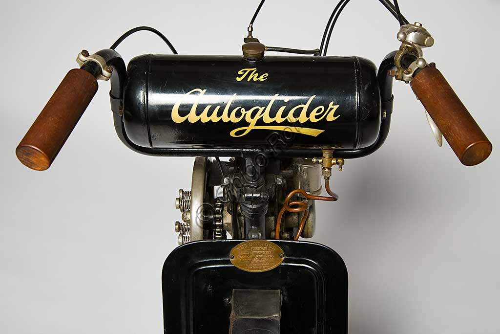 Moto d'epoca Autoglider. Scooter.Marca: Townsend Engineering Companymodello: Autoglider nazione: Regno Unito - Birminghamanno: 1919condizioni: restauratocilindrata: 300motore: monocilindrico a due tempi cambio: Dando seguito al grande senso di libertà che seguì la fine della Grande Guerra, e alla conseguente voglia di spostarsi liberamente, il 1919 segnò in Gran Bretagna una stagione di grande successo popolare per gli scooter e le moto in genere.L' Autoglider fu costruito a Birmingham da Charles Ralph Townsend dapprima nel Model A, senza sella. Ma questo modello che obbligava alla posizione in piedi, non ebbe successo. Poi nei successivi modelli con una piccola e curvilinea carrozzeria in legno compensato che sorreggeva la sella fungendo anche da vano portaoggetti come negli scooter attuali. Poteva montare un motore Villiers di 269 cc, oppure, come in questo caso, un motore Union di 300 cc.Conobbe una certa diffusione e lo si riconosce spesso in molte fotografie dell'epoca.