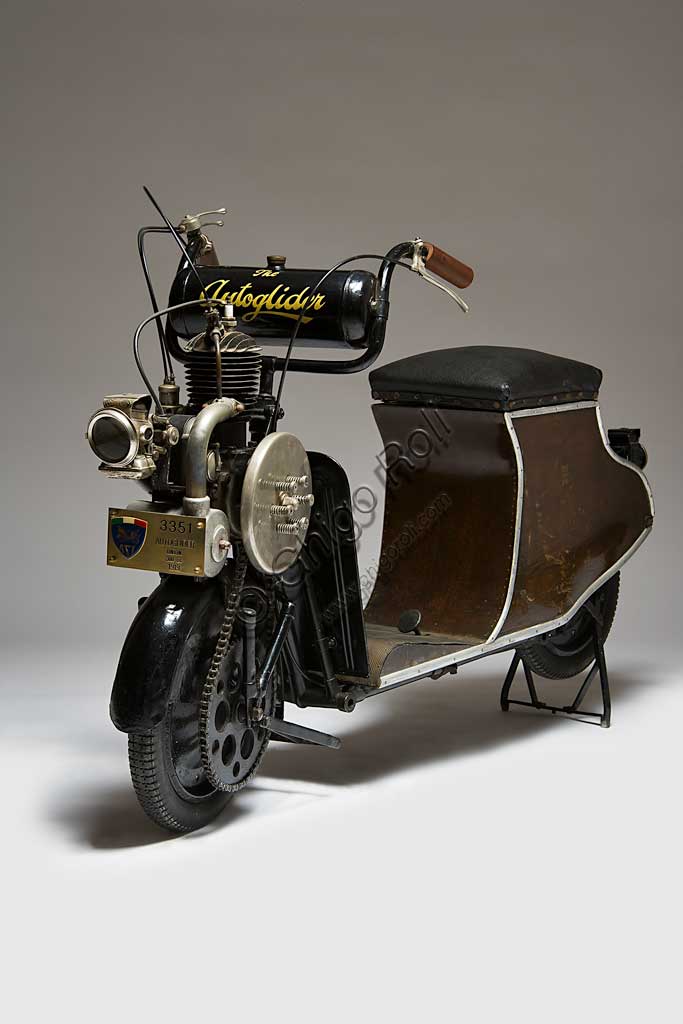 Moto d'epoca Autoglider. Scooter.Marca: Townsend Engineering Companymodello: Autoglider nazione: Regno Unito - Birminghamanno: 1919condizioni: restauratocilindrata: 300motore: monocilindrico a due tempi cambio: Dando seguito al grande senso di libertà che seguì la fine della Grande Guerra, e alla conseguente voglia di spostarsi liberamente, il 1919 segnò in Gran Bretagna una stagione di grande successo popolare per gli scooter e le moto in genere.L' Autoglider fu costruito a Birmingham da Charles Ralph Townsend dapprima nel Model A, senza sella. Ma questo modello che obbligava alla posizione in piedi, non ebbe successo. Poi nei successivi modelli con una piccola e curvilinea carrozzeria in legno compensato che sorreggeva la sella fungendo anche da vano portaoggetti come negli scooter attuali. Poteva montare un motore Villiers di 269 cc, oppure, come in questo caso, un motore Union di 300 cc.Conobbe una certa diffusione e lo si riconosce spesso in molte fotografie dell'epoca.