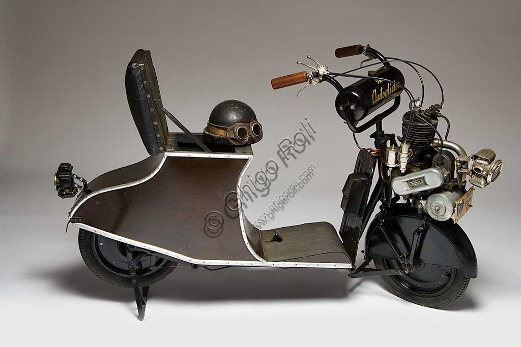 Moto d'epoca Autoglider. Scooter.Marca: Townsend Engineering Companymodello: Autoglider nazione: Regno Unito - Birminghamanno: 1919condizioni: restauratocilindrata: 300motore: monocilindrico a due tempi cambio: Dando seguito al grande senso di libertà che seguì la fine della Grande Guerra, e alla conseguente voglia di spostarsi liberamente, il 1919 segnò in Gran Bretagna una stagione di grande successo popolare per gli scooter e le moto in genere.L' Autoglider fu costruito a Birmingham da Charles Ralph Townsend dapprima nel Model A, senza sella. Ma questo modello che obbligava alla posizione in piedi, non ebbe successo. Poi nei successivi modelli con una piccola e curvilinea carrozzeria in legno compensato che sorreggeva la sella fungendo anche da vano portaoggetti come negli scooter attuali. Poteva montare un motore Villiers di 269 cc, oppure, come in questo caso, un motore Union di 300 cc.Conobbe una certa diffusione e lo si riconosce spesso in molte fotografie dell'epoca.