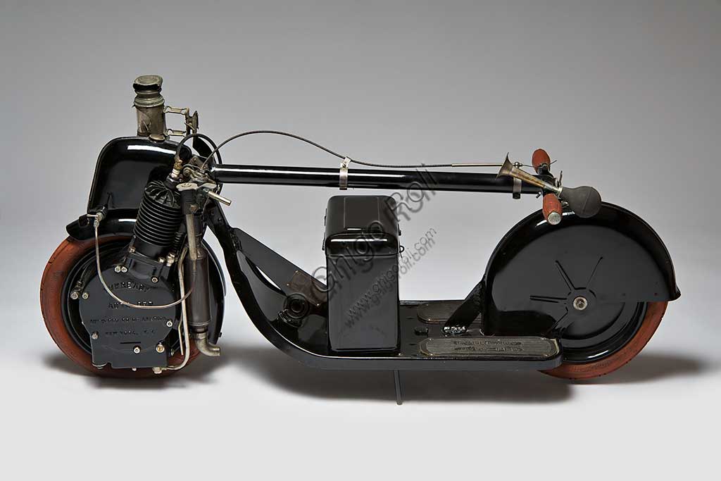 Moto d'epoca Autoped. Scooter.Marca: AUTOPED Companynazione: U.S.A. -Long Island City - NYanno: 1915condizioni: restauratocilindrata: 155 ccmotore: monocilindrico a quattro tempicambio: monomarcia con frizioneScooter significa monopattino e l'Autoped, considerato il primo scooter della storia, non è altro che questo: un piccolo, agile e innovativo monopattino a motore. Concepito per spostamenti sulle brevi distanze, l'Autoped obbligava il pilota a stare in piedi. Il montante del manubrio comandava partenza e arresto: se spinto in avanti rilasciava la frizione, se tirato indietro azionava il freno (e il pensiero va immediatamente al moderno Segway...). Una leva comandava la potenza. Completavano la dotazione un fanale, un klaxon e una cassettina degli attrezzi. Il manubrio era ripiegabile, consentendo di spstare a mano e riporre in poco spazio questo piccolo gioiello del progresso. Gli pneumatici e le manopole del manubrio davano, con il loro colore arancione, un tocco di assoluta modernità a questo mezzo. In questo esemplare anche le gomme sono originali.