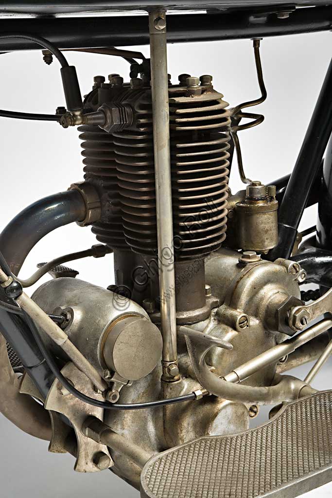 Moto d'epoca Garelli Turismo 350. Motore.Marca: Garellimodello: Turismo 350nazione: Italia - Sesto San Giovannianno: 1926condizioni: restauratacilindrata: 349 (alesaggio e corsa 50 x 89 x 2) ccmotore: due tempi a cilindro sdoppiato in unico bloccocambio: in blocco con la frizione, a due velocità con selettore sul serbatoioFondata nel 1919 dal brillante ingegnere Adalberto Garelli, che aveva già lavorato alla Bianchi e alla Stucchi, la Garelli iniziò a vincere competizioni a man salva con il primo e unico prototipo prima ancora di iniziare la produzione. Cominciò con la Genova Trieste - Genova, poi con il Raid Nord - Sud dello stesso anno e fu una delle moto più veloci per tutti gli anni '20. Il suo motore a due tempi adotta uno schema del tutto inusuale: doppio cilindro con biella e spinotto unico, testata in bronzo con camera di combustione comune ai due cilindri; utilizza miscela fino al 15% (!) ma ha anche una pompa dell'olio a portata variabile azionata dall'albero motore che immette l'olio nel cilindro destro. 