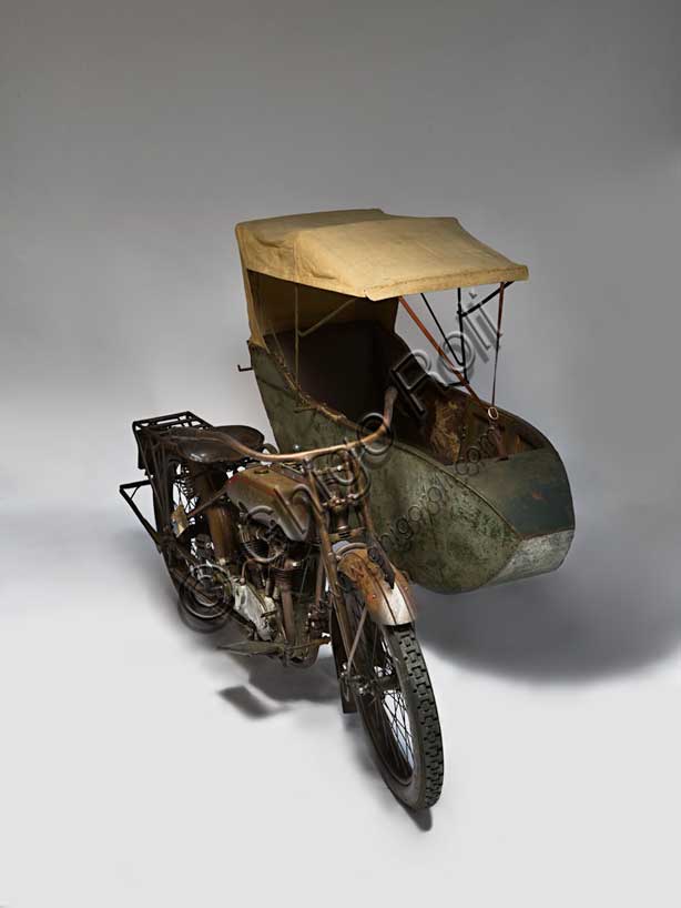 Moto d'epoca “Harley-Davidson T - Side”Marca: Harley-Davidsonmodello: T Sidenazione: U.S.A. - Milwaukeeanno: 1917condizioni: conservatacilindrata: 1000 (alesaggio e corsa 84,1 x 88,9)motore: bicilindrico a V di 45°cambio: a tre rapportiFondata nel 1903 la H-D ha accompagnato tutta la storia degli Stati Uniti fino ad oggi, dalle prime moto militari usate nelle schermaglie di confine contro Pancho Villa, alle grandi forniture per l'esercito che nel 1917 era entrato in guerra sul fronte europeo, dai mezzi da lavoro (i "tricicli" dei lattai e dei postini americani) alle grandi bicilindriche della polizia. Già nel '20 era il primo produttore di motociclette al mondo.Questo elegante sidecar del 1917, integralmente conservato e perfettamente funzionante, mostra già il bicilindrico a V che caratterizza ancor oggi la produzione della Harley. Ha distribuzione a valvole contrapposte (scarico laterale, aspirazione in testa).