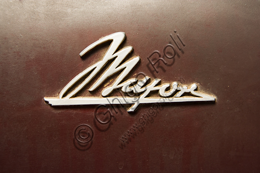 Moto d'epoca Mayor. Marchio.Marca: Mayornazione: Italia - Torinoanno: 1947condizioni: conservatacilindrata: 349,3 cc. (alesaggio e corsa 76 x 77)motore: monocilindrico verticale a valvole in testacambio: in blocco a quattro rapporti con comando a pedalee trasmissione finale ad alberoSi deve a Salvatore Maiorca, (da cui anche il nome della moto) brillante ingegnere assai noto a Torino, uno dei progetti più avveniristici di tutta la storia della motocicletta. La Mayor, di cui sopravvive questo unico prototipo, costruito nelle officine Aeritalia del gruppo Fiat e pensato probabilmente per la polizia municipale. Ha carrozzeria portante e avvolgente che integra faro e parafanghi, sterzo indiretto, motore di derivazione aeronautica raffreddato ad aria forzata, albero motore longitudinale che si prolunga nel cambio in blocco e nella trasmissione ad albero. Ma la caratteristica più innovativa per cui la Mayor sarà ricordata, anche se non ebbe seguito, sono le ruote elastiche: un disco d'acciaio unisce per mezzo di tamponi in gomma il cerchio esterno al mozzo interno garantendo, almeno in teoria, il molleggio della moto senza bisogno di altre sospensioni. 