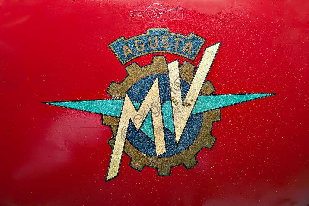 Moto d'epoca MV Agusta 125 Monoalbero Corsa. Marchio.Marca: MV Agustamodello: 125 Monoalbero Corsanazione: Italia - Schiranna (VA)anno: 1954condizioni: conservatacilindrata: 123,5 (alesaggio e corsa 53 x 56)motore: monocilindrico, albero a cammes in testacambio: a quattro rapportiLa storica azienda fondata nel 1907 dal Conte Giovanni Agusta, nota per la produzione aeronautica, iniziò a produrre motociclette con il figlio Domenico solo nel '46, con il nome Meccanica Verghera (MV). Dopo le prime 98, nelle versioni Turismo e Sport, costruisce moto sempre più orientate verso le competizioni; questo esemplare, che toccava i 150 km/h, ne è una delle prime testimonianze.E' appena il caso di ricordare che, la MV con  75 campionati del mondo e 270 Gran Premi vinti, è la marca più vittoriosa della storia del motociclismo. Un record nei record: con Giacomo Agostini, vinse ininterrottamente il campionato del mondo dal 1967 al 1973 sia nella classe 350 che nella 500.