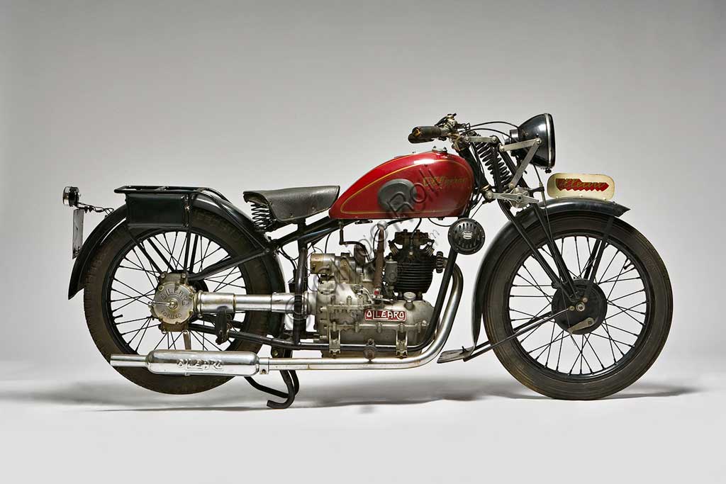 Moto d'epoca Ollearo Tipo Quattro 175Marca: Ollearomodello: Tipo Quattro 175nazione: Italia - Torinoanno: 1932condizioni: restauratacilindrata: 175 (alesaggio e corsa 60 x 61,5)motore: Monocilindrico a quattro tempi e valvole in testacambio: in blocco, a quattro rapporti Neftali Ollearo apre l'attività di costruttore nel 1923 in Corso Valentino mettendo a punto una bicicletta a motore di 131 cc. e, in pochi anni, è già conosciuto per l'alta qualità e le raffinate soluzioni tecniche delle sue moto. Questa Tipo Quattro di 175 cc. ha, rara tra le moto italiane, trasmissione finale ad albero e giunti cardanici. Il cambio, novità per quegli anni, è già in un unico blocco con il motore. Monta freni a tamburo su ogni ruota.Costa, all'uscita nel 1930, 5900 Lire, ridotte a 4750 nel 1933. La pubblicità recita: "La prima moto e l'unica che accomuna stabilità, sicurezza e comodità, sin ora sconosciute"... L'azienda, con l'entrata in guerra dell'Italia e le conseguenti restrizioni alla circolazione, produrrà solo motofurgoni e motocarri. 