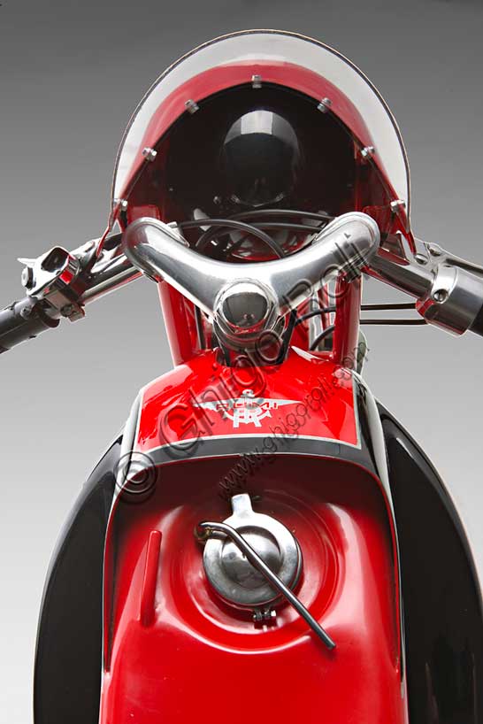 Moto d'epoca “Rumi Junior 125”Marca: Fonderie Officine Rumimodello: Junior 125nazione: Italia - Bergamoanno: 1956condizioni: restauratacilindrata: 124,6 (alesaggio e corsa 42 x 45)motore: bicilindrico orizzontale due tempicambio: in blocco a quattro rapportiDonnino Rumi subentra al padre nella fonderia per bronzo da questi creata. Durante la Seconda Guerra Mondiale rifiuta di convertire la produzione a scopi bellici e diventa partigiano latitante. Nel dopoguerra, alla domanda di mezzi di trasporto economici, risponde affiancando la produzione di motoleggere a quella già avviata di macchine tessili e per pastifici. Con l'aiuto dell'amico progettista nautico Pietro Vassena, nel 1949 è in grado di presentare al salone di Milano la prima, innovativa, motocicletta Rumi.La Junior deriva dalla "Bicarburatore" monta una forcella Earles, ed è fin dall'inizio destinata alle corse. Viene venduta a corridori privati sia italiani che stranieri e, grazie alla sua agilità, riscuote grande successo.