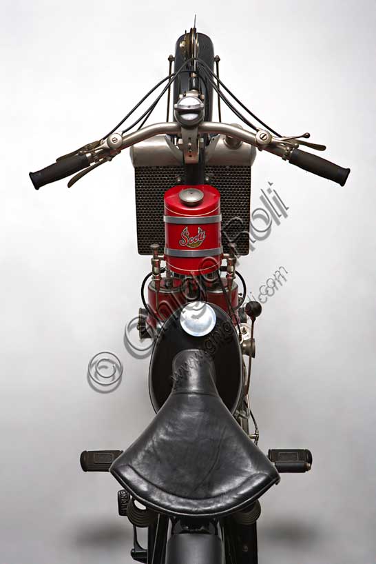 Vintage motorcycle “Scott Super Squirrel”Brand: Scottmodel: Super Squirrelcountry: United Kingdom - Shipleyyear: 1926 (?)condition: restoreddisplacement: 596engine: two-stroke twin-cylinder water-cooledgearbox: two-speedFounded in Shipley, Yorkshire, by Alfred Angus Scott, creator of more than fifty patents, the Scott factory produced motorcycles from 1909 to 1933. Several particularly innovative solutions were adopted in series production. The Scott was the first motorcycle to adopt water cooling. Some construction choices such as the open triangle frame, allowing the vehicle to be used by a female public, seemed to indicate the desire to address a “relaxed” user base. Despite this, the Scott soon proved to be a fast and efficient motorcycle, collecting numerous sporting successes. It reached 105 km/h. It won the Tourist Trophy in 1912 and 1913.