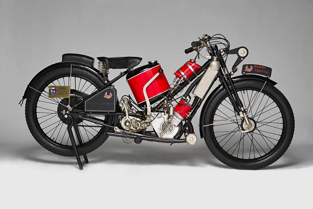 Moto d'epoca Scott Super Squirrel.Marca: Scottmodello: Super Squirrelnazione: Regno Unito - Shipleyanno: 1926 (?)condizioni: restauratacilindrata: 596motore: bicilindrico a due tempi raffreddato ad acquacambio: a due marceFondata a Shipley, nello Yorkshire, da Alfred Angus Scott, ideatore di più di cinquanta brevetti, la fabbrica Scott produsse motociclette dal 1909 fino al 1933. Nella produzione di serie vennero adottate diverse soluzioni particolarmente innovative. La Scott fu la prima moto ad adottare il raffreddamento ad acqua. Alcune scelte costruttive come il telaio a triangolo aperto, consentendo l’utilizzo del mezzo ad un pubblico femminile, sembravano indicare la volontà di rivolgersi ad una utenza “tranquilla”. Nonostante questo la Scott si rivelò presto una motocicletta veloce ed efficace, raccogliendo numerosi successi sportivi. Raggiungeva i 105 km/h. Vinse il Tourist Trophy. nel 1912 e nel 1913.