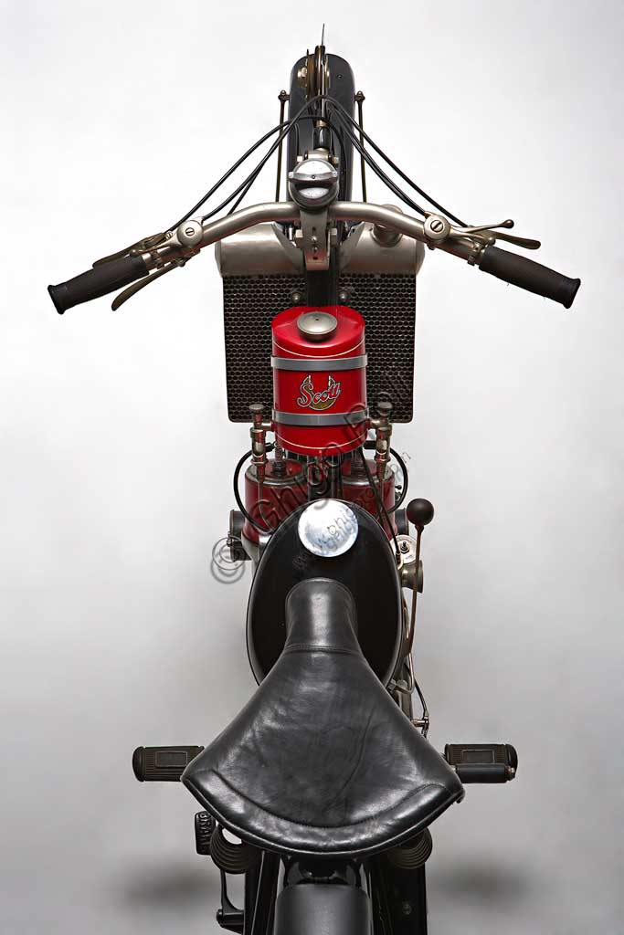 Moto d'epoca Scott Super Squirrel.Marca: Scottmodello: Super Squirrelnazione: Regno Unito - Shipleyanno: 1926 (?)condizioni: restauratacilindrata: 596motore: bicilindrico a due tempi raffreddato ad acquacambio: a due marceFondata a Shipley, nello Yorkshire, da Alfred Angus Scott, ideatore di più di cinquanta brevetti, la fabbrica Scott produsse motociclette dal 1909 fino al 1933. Nella produzione di serie vennero adottate diverse soluzioni particolarmente innovative. La Scott fu la prima moto ad adottare il raffreddamento ad acqua. Alcune scelte costruttive come il telaio a triangolo aperto, consentendo l’utilizzo del mezzo ad un pubblico femminile, sembravano indicare la volontà di rivolgersi ad una utenza “tranquilla”. Nonostante questo la Scott si rivelò presto una motocicletta veloce ed efficace, raccogliendo numerosi successi sportivi. Raggiungeva i 105 km/h. Vinse il Tourist Trophy. nel 1912 e nel 1913.