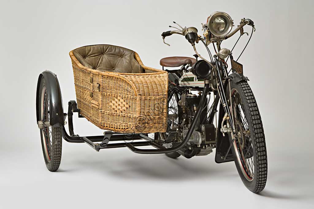 Moto d'epoca Triumph H SideMarca: Triumphmodello: H Sidenazione: Regno Unito - Coventryanno: 1918condizioni: restauratocilindrata: 550,1 (alesaggio e corsa 85 x 97)motore: quattro tempi a valvole lateralicambio: Sturmey Archer a tre rapportitrasmissione finale a cinghiaDopo aver prodotto biciclette per alcuni anni, nel 1902 la Triumph, casa fondata da tre immigrati tedeschi, costruisce la sua prima bicicletta a motore con motorizzazione Minerva. A questa fanno seguito alcuni modelli sempre motorizzati da altri, fino al  1905 quando inizia la produzione della prima motocicletta costruita interamente in casa Triumph.  Nel 1915 esce il modello H, di cui qui presentiamo un elegante esemplare con motocarrozzetta. Monta un motore disegnato da Mauritz Schülte, uno dei tre soci, ed è concepita per l'esercito. Si rivela però talmente affidabile e piacevole da condurre che, nel dopoguerra, conoscerà una grande diffusione anche tra i privati, dando inizio a quel successo che farà della Triumph una delle più prestigiose marche britanniche.