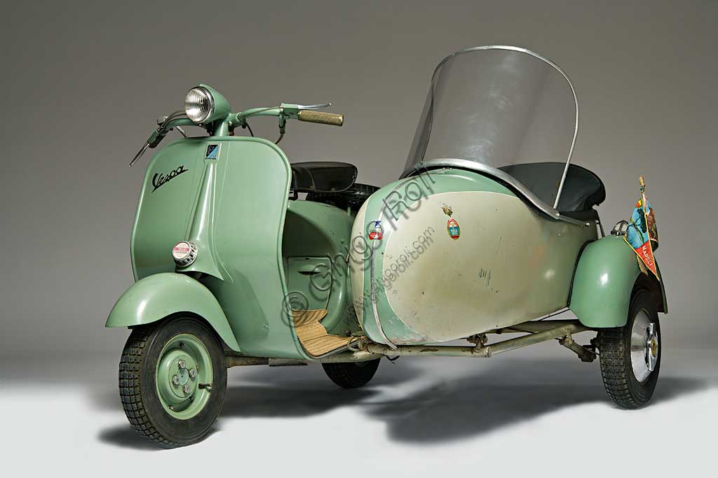 Moto d'epoca Vespa 125 U Sidecar. Scooter.Marca: Piaggiomodello: Vespa 125 U Sidecarnazione: Italia - Genova - Pontederaanno: 1953condizioni: conservatacilindrata: 124,2motore: monocilindrico a due tempicambio: al manubrio a tre rapportiLa Vespa "U", la prima con faro al manubrio, fu un modello economico, prodotto per un ipotetico pubblico che voleva risparmiare le circa ventimila lire in meno rispetto alla Vespa 125 allora in catalogo.Nonostante questo non incontrò i favori del pubblico e usci di produzione dopo poco più di un anno. Questo ne fa un modello piuttosto raro e ricercato dai collezionisti.Ancora più rara è questa versione con sidecar, tanto più che monta una delle poche carrozzette originali Piaggio, distinguibile dal telaio a braccio unico, quando la maggior parte dei sidecar veniva costruita da allestitori locali e aveva telaio a tre tubi.