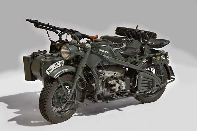Moto d'epoca “Zündapp KS”Marca: Zündappmodello: KSnazione: Germaniaanno: 1942condizioni: restauratacilindrata: 750 cc.motore: bicilindrico boxercambio: a 4 rapporti e retromarcia, trasmissione ad albero, due ruote posteriori motrici, con differenziale ripartitore e bloccabileFondata nel '17 dalla Friederich Krupp AG e dall'ing. Fritz Neumeyer come fabbrica di  macchine utensili (Zunder und Apparatebau GmbH) la Zündapp viene presto convertita alla sola produzione di motociclette. Dal 1940 la produzione si concentra sulle moto militari per la Wehrmacht. Di questa produzione il sidecar qui raffigurato è il modello più prodotto con 18.000 esemplari costruiti. Il telaio (rigido) fu disegnato da Ferdinand Porsche. Ruote e freni sono di produzione BMW. Anche il carrozzino, fornito da ditte esterne, è uguale a quello BMW per fini di unificazione richiesti dall'esercito.
