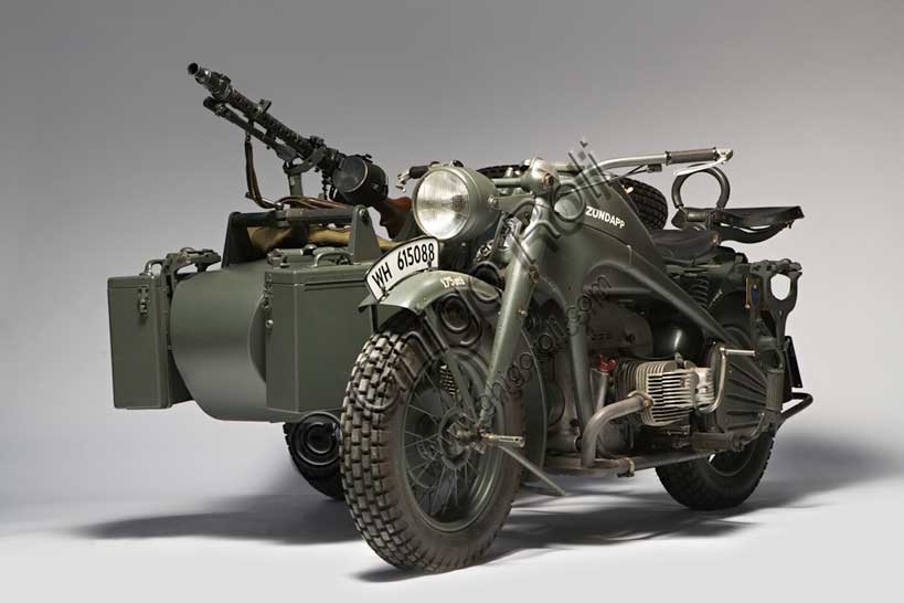 Moto d'epoca “Zündapp KS”Marca: Zündappmodello: KSnazione: Germaniaanno: 1942condizioni: restauratacilindrata: 750 cc.motore: bicilindrico boxercambio: a 4 rapporti e retromarcia, trasmissione ad albero, due ruote posteriori motrici, con differenziale ripartitore e bloccabileFondata nel '17 dalla Friederich Krupp AG e dall'ing. Fritz Neumeyer come fabbrica di  macchine utensili (Zunder und Apparatebau GmbH) la Zündapp viene presto convertita alla sola produzione di motociclette. Dal 1940 la produzione si concentra sulle moto militari per la Wehrmacht. Di questa produzione il sidecar qui raffigurato è il modello più prodotto con 18.000 esemplari costruiti. Il telaio (rigido) fu disegnato da Ferdinand Porsche. Ruote e freni sono di produzione BMW. Anche il carrozzino, fornito da ditte esterne, è uguale a quello BMW per fini di unificazione richiesti dall'esercito.