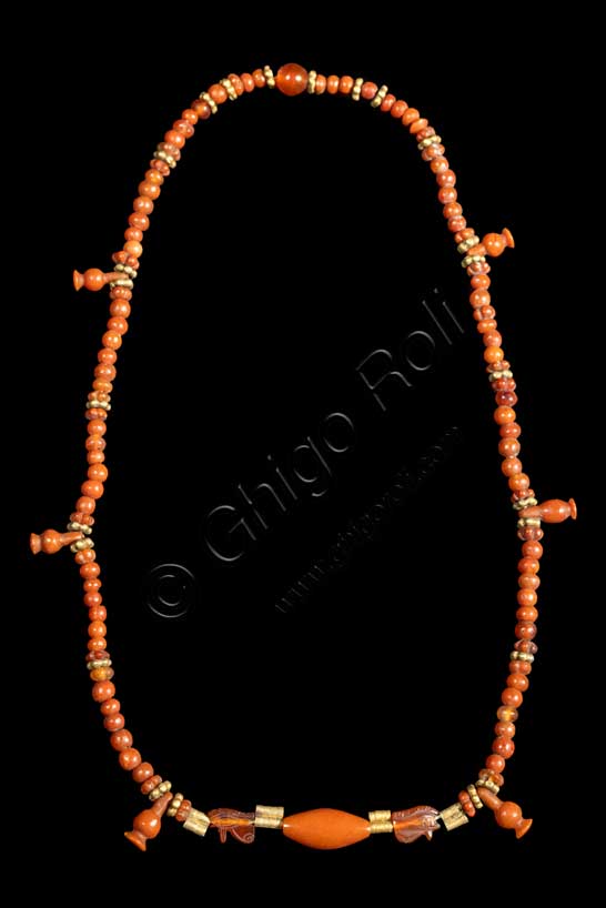 Museo Civico Archeologico di Bologna: collana con melagrane.  Nuovo Regno: XVIII-XX dinastia (1539-1075 a.C.).Inventario EG 3103 La collana, costituita da vaghi configurati a melagrana e a rosetta, da perline sferiche e tubicini in corniola, ai quali si alternano tubicini e rosette in oro, ha al centro un vago ovoidale tra due occhi udjat del dio Horo affrontati, simboli di integrità. Al suo frutto, ricco di chicchi succosi, gli Egiziani associano da subito l'idea della fertilità e della rinascita, e perciò indossare una collana come questa era propiziatorio di una lunga vita, terrena o ultraterrena. Anche la scelta della corniola, simile nel colore alle tonalità arancio-rossastre della melagrana, ne rafforzava la valenza magica.