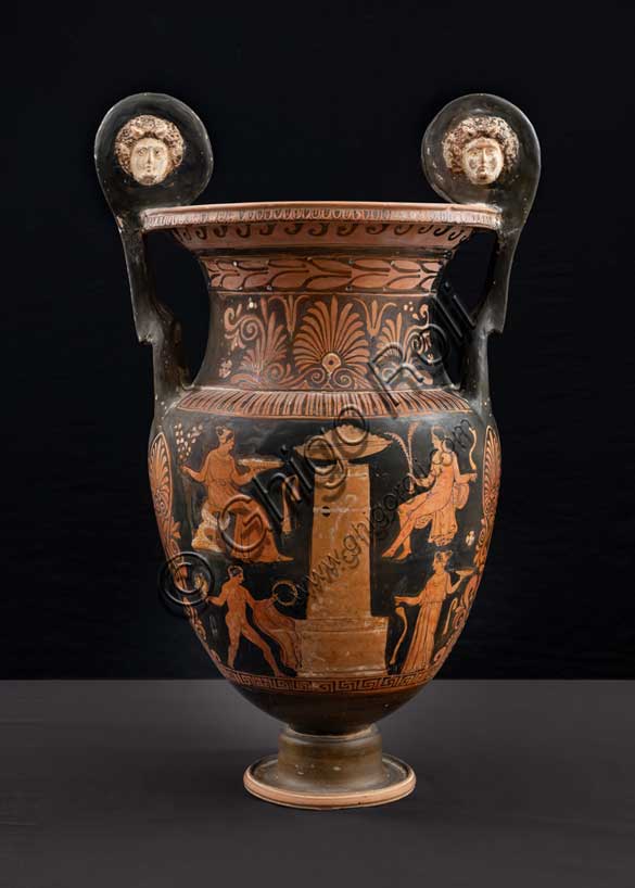 Museo Civico Archeologico di Bologna: Cratere a figure rosse apulo a volute con mascheroni.Lato B: scena funeraria: al centro stele funeraria, decorata da una tenia e da un meandro ad onda in bianco; alla sua sommità è posta una grande coppa piena di offerte. Ai lati della stele, volte verso di essa e disposte simmetricamente su due piani sono quattro figure.340 - 320 a.C.Inv. G_0392