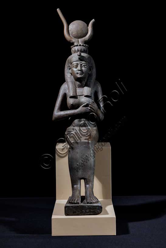 Museo Civico Archeologico di Bologna: Isi (Iside) seduta in trono.Statuetta di Epoca Tarda: XXVI-XXX dinastia (664-342 a.C.). Bronzo con agemina in oro.Inventario EG 248/9.Fra tutte le divinità femminili del pantheon egiziano Isi è la dea per eccellenza, la più conosciuta, “la grande di magia”, soprattutto durante l’Antico Regno (2705-2225 a.C.), quando il suo nome e la sua immagine compaiono raramente sugli edifici religiosi e nei luoghi di culto domestico. Introdotta con un ruolo da protagonista nella leggenda di Osiri, forse attorno al 2500 a.C., le caratteristiche di grande maga si affiancano ad altre più umane, che permettono al suo culto di sopravvivere all'Egitto faraonico, diffondendosi dal VI secolo a.C. in tutto il bacino del Mediterraneo. Isi si identifica così con la fedele compagna del dio Osiri, esperta nell'arte di assecondarlo, di preparane le esequie, di perpetuarne il culto dopo la morte, così come con il prototipo ideale della donna egiziana che veglia sul proprio figlio Horo, erede al trono di Osiri. La dea, raffigurata in questo bronzetto nel suo ruolo di madre premurosa, siede in trono e porge il seno al figlio Horo, ora scomparso. Alla semplicità della veste, una tunica aderente che esalta le linee sinuose del corpo femminile, si contrappongono la ricchezza degli occhi in agemina, la ieraticità della corona hathorica dal tipico disco solare tra corna bovine a lira e il volume dell’acconciatura a tre bande di capelli, sormontata dalla spoglia di avvoltoio. 