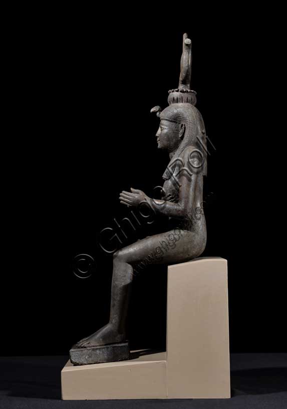 Museo Civico Archeologico di Bologna: Isi (Iside) seduta in trono.Statuetta di Epoca Tarda: XXVI-XXX dinastia (664-342 a.C.). Bronzo con agemina in oro.Inventario EG 248/9.Fra tutte le divinità femminili del pantheon egiziano Isi è la dea per eccellenza, la più conosciuta, “la grande di magia”, soprattutto durante l’Antico Regno (2705-2225 a.C.), quando il suo nome e la sua immagine compaiono raramente sugli edifici religiosi e nei luoghi di culto domestico. Introdotta con un ruolo da protagonista nella leggenda di Osiri, forse attorno al 2500 a.C., le caratteristiche di grande maga si affiancano ad altre più umane, che permettono al suo culto di sopravvivere all'Egitto faraonico, diffondendosi dal VI secolo a.C. in tutto il bacino del Mediterraneo. Isi si identifica così con la fedele compagna del dio Osiri, esperta nell'arte di assecondarlo, di preparane le esequie, di perpetuarne il culto dopo la morte, così come con il prototipo ideale della donna egiziana che veglia sul proprio figlio Horo, erede al trono di Osiri. La dea, raffigurata in questo bronzetto nel suo ruolo di madre premurosa, siede in trono e porge il seno al figlio Horo, ora scomparso. Alla semplicità della veste, una tunica aderente che esalta le linee sinuose del corpo femminile, si contrappongono la ricchezza degli occhi in agemina, la ieraticità della corona hathorica dal tipico disco solare tra corna bovine a lira e il volume dell’acconciatura a tre bande di capelli, sormontata dalla spoglia di avvoltoio. 